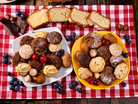 Oatmeal Cookies and sand chocolate cake with blueberries on wooden table with gingham cloth in farm style close up. Table setting breakfast for two with cups in. Best range of confectionery products.の写真素材