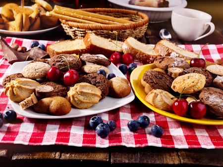 Oatmeal Cookies and sand chocolate cake with blueberries on wooden table with gingham cloth in farm style close up. Table setting breakfast for two with cups in. Cozy, homely atmosphere.の写真素材
