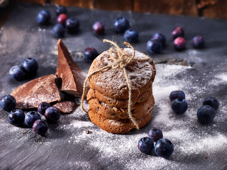 Serving food on slate onto wooden table. Oatmeal cookies biscuit with blueberry on picnic dark tiles countrylike. Chocolate Xmas holiday chip cookies tied with string.の写真素材