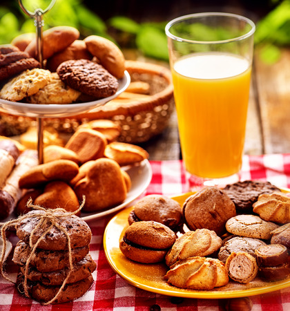 Chocolate oatmeal cookies and sand heart shape cake on plate table with fresh orange juice glass drink in farm style. Table setting breakfast on gingham tablecloth. Selection of beautiful snacks.の写真素材