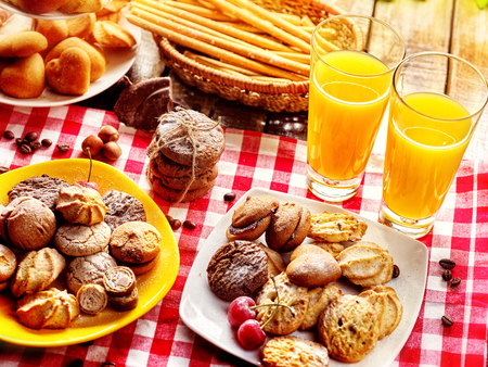Chocolate oatmeal cookies and sand heart shape cake on plate table with fresh orange juice glass drink in farm style. Table setting breakfast on gingham tablecloth. Top view family dinner.の写真素材