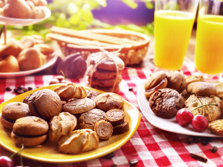 Chocolate oatmeal cookies and sand heart shape cake on plate table with fresh orange juice glass drink in country style. Rural table setting breakfast on gingham tablecloth.の写真素材