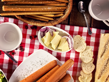 Sausage portion with bread baguette on table setting on checkered tablecloth and cup in farm style. Composition of meat products. Recipes from home cooking.の写真素材