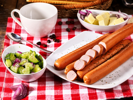 Sausage portion with bread baguette on table setting on checkered tablecloth and cup in farm style. Best assortment of meat products.の写真素材