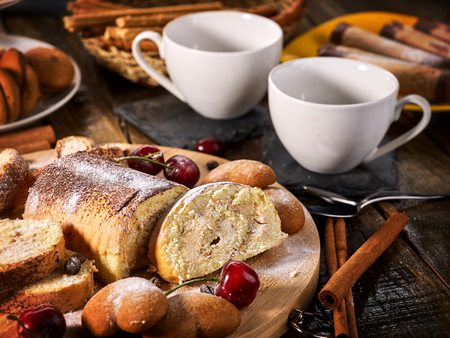 Rolled biscuit and sand chocolate cookies on board. Cinnamon stick and cherry on kitchen wood table in rustic style. Easily digestible and quickly digestible substances.の写真素材