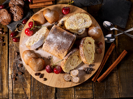 Sand nut chocolate cookies and rolled biscuit on board and cinnamon stick and straw pastry on kitchen on wood table in rustic style top view. Cups of tea and dessert spoon. Top view.の写真素材