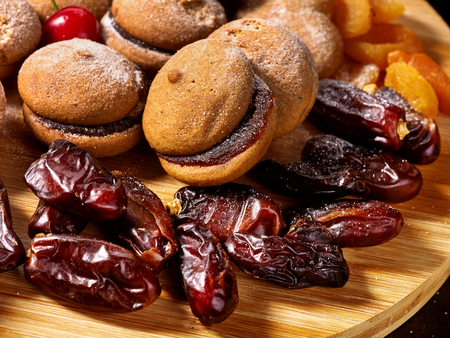 Oatmeal cookies and sand chocolate cake with cherry berry and dried fruits dates, apricots on cutting board on wooden table in rustic style.の写真素材