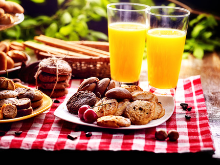 Chocolate oatmeal cookies and sand heart shape cake on plate table with fresh orange juice glass drink in farm style. Table setting breakfast on gingham tablecloth. Homemade, delicious recipes.の写真素材