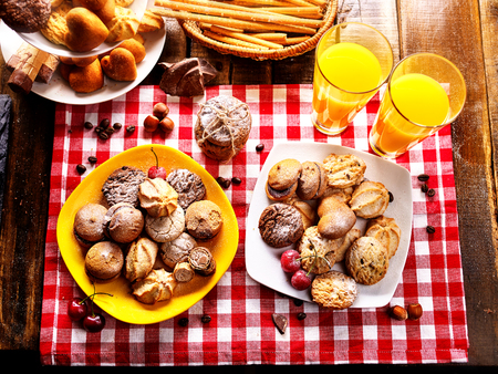 Chocolate oatmeal cookies and sand heart shape cake on plate table with fresh orange juice glass drink summer outdoor in farm wooden style. Table setting breakfast on gingham tablecloth top view.の写真素材