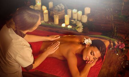 Masseuse give a massage to woman in spa salon with candles and sun flare.の写真素材