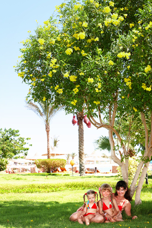 Mother woman with two children girl relax on green grass in hotel with park and sea on vacation.の写真素材