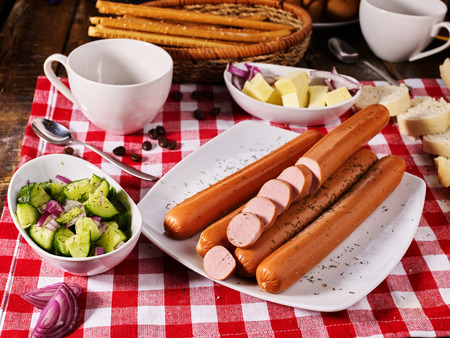 Sausage portion with bread baguette on table setting on checkered tablecloth and cup in farm style. How and from what make sausages.の写真素材