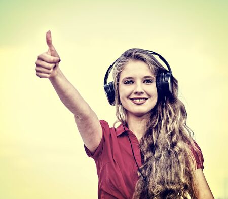 Student girl in headphone listen music after exam and show thumb up. Time to relaxin street city sepia tone image .の写真素材
