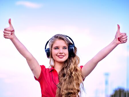 Student girl in headphone listen music and show thumb up after exam. Time to relaxin street city.の写真素材