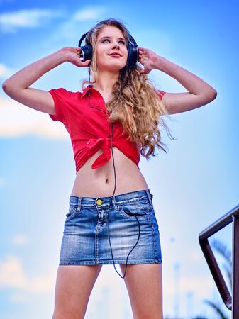 Student girl wearing in denim miniskirt and headphone listen music after exam. Time to relaxin street city.の写真素材