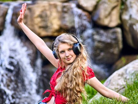 Student girl with backpack in headphone listen music after exam. Time to relaxing on green grass near waterfall nature. Strong immune system depends on many factors.の写真素材