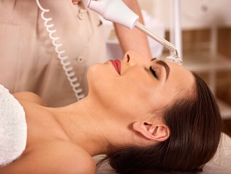 Facial treatment procedures darsenval. Close up of young woman with female beautician does face skin care stimulator.の写真素材