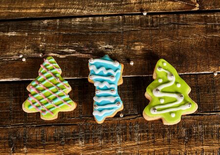 Decorative Christmas cookies sparse on wooden board table. Top view of three horizontal ginger biscuits Xmas tree with icing on square frame.の写真素材