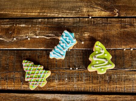 Decorative Christmas cookies sparse on wooden board background. Top view of three ginger biscuits Xmas tree with icing on square frame.の写真素材