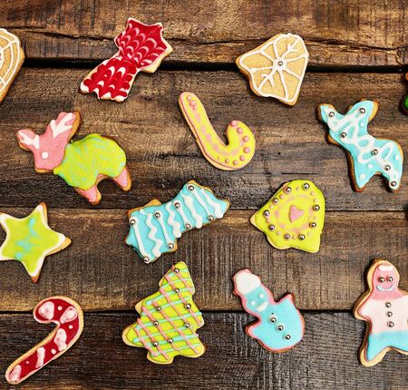 Decorative Christmas cookies sparse on wooden board background. Top view of ginger biscuits Xmas tree and gingerbread man with icing on square frame.の写真素材