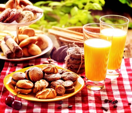 Chocolate oatmeal cookies and sand heart shape cake on plate table with fresh orange juice glass drink in farm style. Table setting breakfast on gingham tablecloth. Perfect product. Dessert in cafe.の写真素材