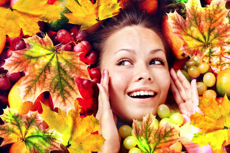 Autumn leaves background with beauty face and hands of beautiful woman. Fashion dream in red fall color outside.の写真素材