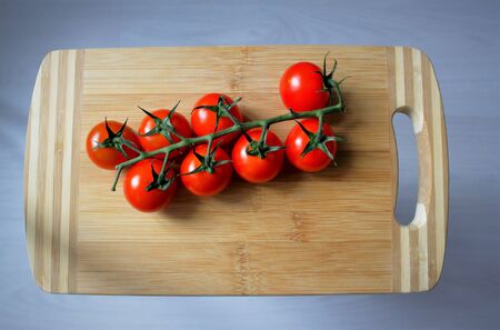 branch of cherry tomatoes on a wooden board and gray backgroundの写真素材
