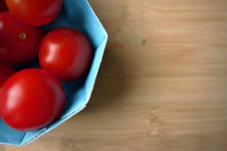 blue basket with bright red cherry tomatoes on a wooden board background