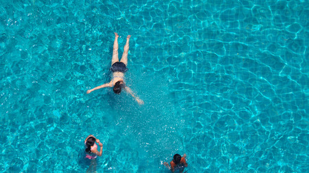 People swimming in the hotel pool that have blue water and sun light reflect on it and top view...
