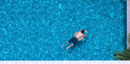 People swimming in the hotel pool in summer sunlight with blue color water and top view angle.