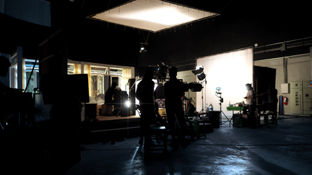 Silhouette of people working in big production studio for shooting or recording movie video by digital camera and lighting set.の写真素材
