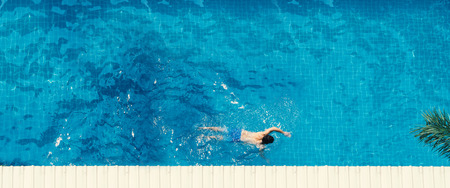 Swimming pool top view angle which young man relaxing and enjoying in pools of his hotel in summer season of Thailand at vacation day and have sun light and flares on blue water surface.の写真素材