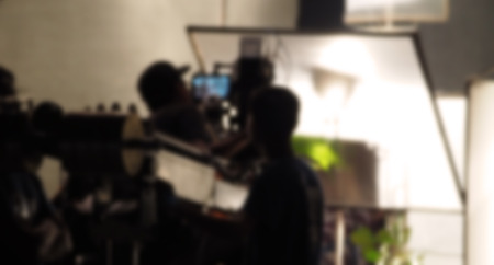 Blurred images of behind the scenes of filming or movie shooting or video production for online commercial and crew teams setting up light and prop and blue screen for next shot of camera recordingの写真素材