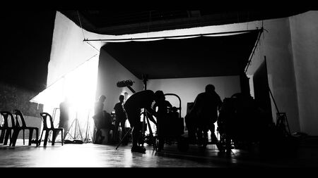 Behind the shooting of video online commercial production and film crew team working and setting light or camera or soft box and equipment set up in big studio in silhouette styleの写真素材