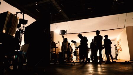 Behind the shooting video production and lighting set for filming which movie crew team working and silhouette shadow of camera and professional equipment in big studio for commercial advertising.の写真素材