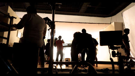 Behind the shooting video production and lighting set for filming which movie crew team working and silhouette shadow of camera and professional equipment in big studio for commercial advertising.の写真素材