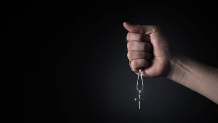 Close-up images of crucifix pendant and necklace in hand on black color background in studio which represent praying for god or jesus and thank gods for giving peaceful and faithful to peopleの写真素材