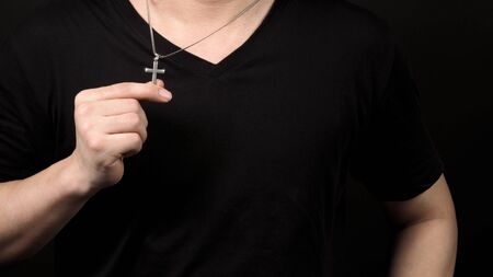 Silver crucifix or cross pendant and necklace on body or hand studio shot black color background...