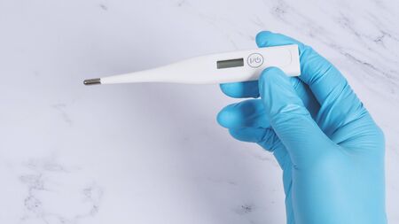 Digital thermometer white color in doctor hands wearing hospital medical gloves light blue color...