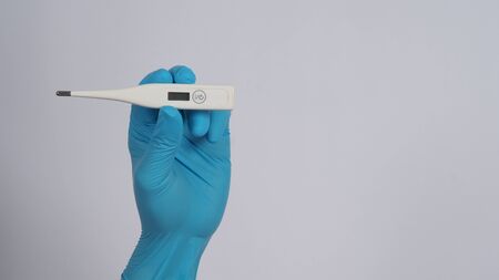 Digital thermometer white color in doctor hands wearing hospital medical gloves light blue color...