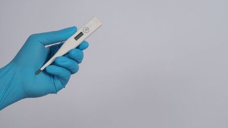 Digital thermometer white color in doctor hands wearing hospital medical gloves light blue color...
