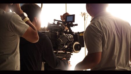 Behind the shooting production crew team and hd video camera and equipment in studio which includes big tripod, soft box light, monitors, lens for making online web film or movie or live broadcastingの写真素材