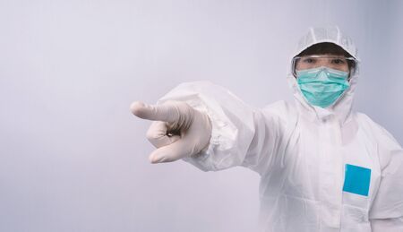 Doctor in PPE suit or Personal Protection Equipment point out to copy space and wearing white color medical rubber gloves and clear goggles glasses and green N95 mask to protect and fight pandemic virusの写真素材