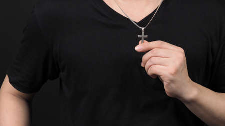 Crucifix pendant or cross sign made from silver and hold in man hand. represent praying for someone that pass away from World pandemic coronavirus and close-up shot black backgroundの写真素材