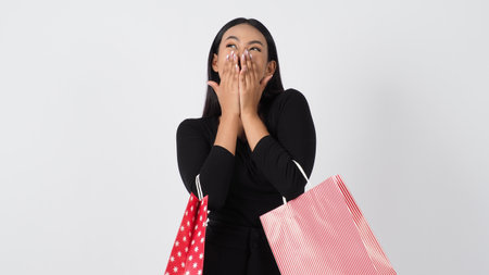 Happy shopping concept. Young asian Thai woman in action or activity of purchasing goods from stores or online shop. Happily girl and shopping bags during sale season in studio white backgroundの写真素材