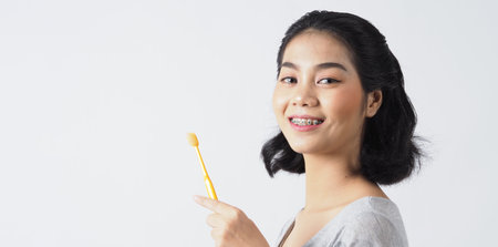 Dental brace teenager girl smile holding toothbrush and looking to camera. white teeth with blue braces. Dental care. Asian woman with contact lens and orthodontic accessories. Cosmetic dentistry. white BGの写真素材