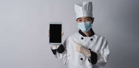 Chef wearing face protective medical mask or respirator for protection from virus disease. Food safety and coronavirus pandemic. chef posing gesture represent online ordering. food healthcare.の写真素材
