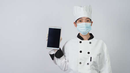 Chef wearing face protective medical mask or respirator for protection from virus disease. Food safety and coronavirus pandemic. chef posing gesture represent online ordering. food healthcare.の写真素材