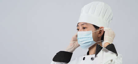 Chef wearing face protective medical mask or respirator for protection from virus disease. Food safety and coronavirus pandemic. chef posing gesture represent online ordering. food healthcare.の写真素材