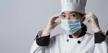 Chef wearing face protective medical mask or respirator for protection from virus disease. Food safety and coronavirus pandemic. chef posing gesture represent online ordering. food healthcare.の写真素材